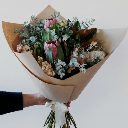 Bouquet of flowers wrapped in brown paper held by a person on a white background. Bendigo Florist.