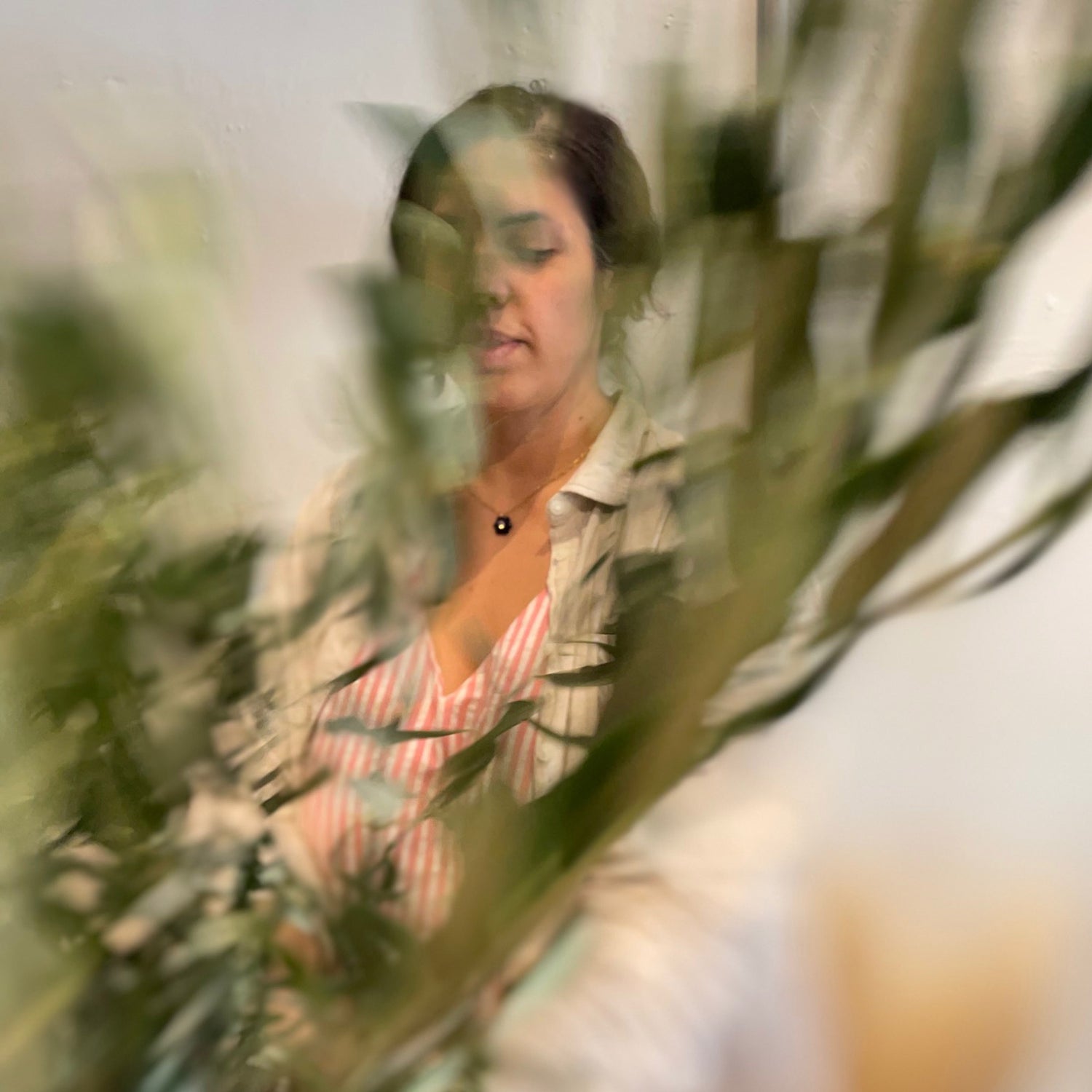 Woman holding olive foliage in cream shirt with a floral necklace designing a bouquet in Bendigo, Australia.