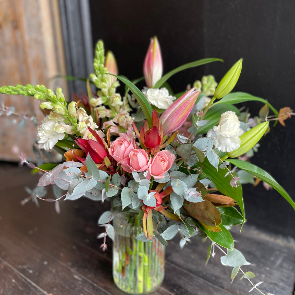 Bold bright flowers in lilies, roses and seasonal flowers in a glass vase. 